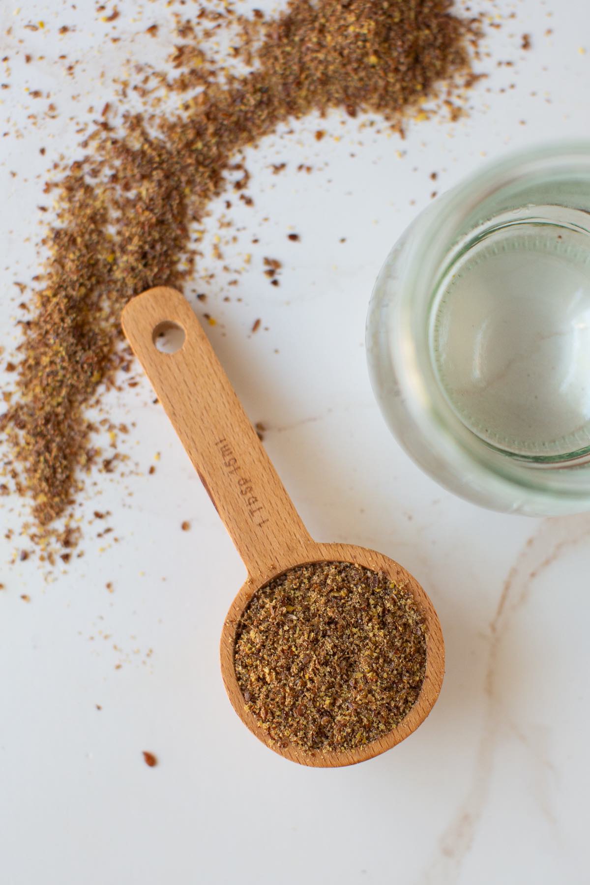 A wooden tablespoon with ground flaxseed meal spilling out on a table.