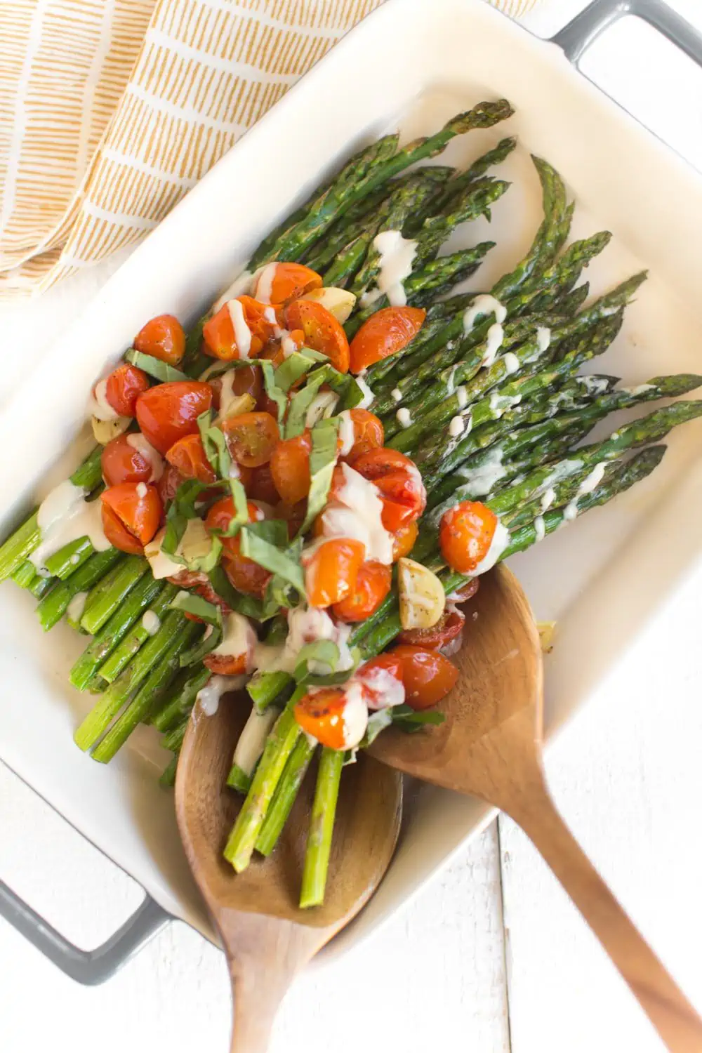 Roasted garlic asparagus with burst tomatoes and tahini drizzle in a baking dish.  
