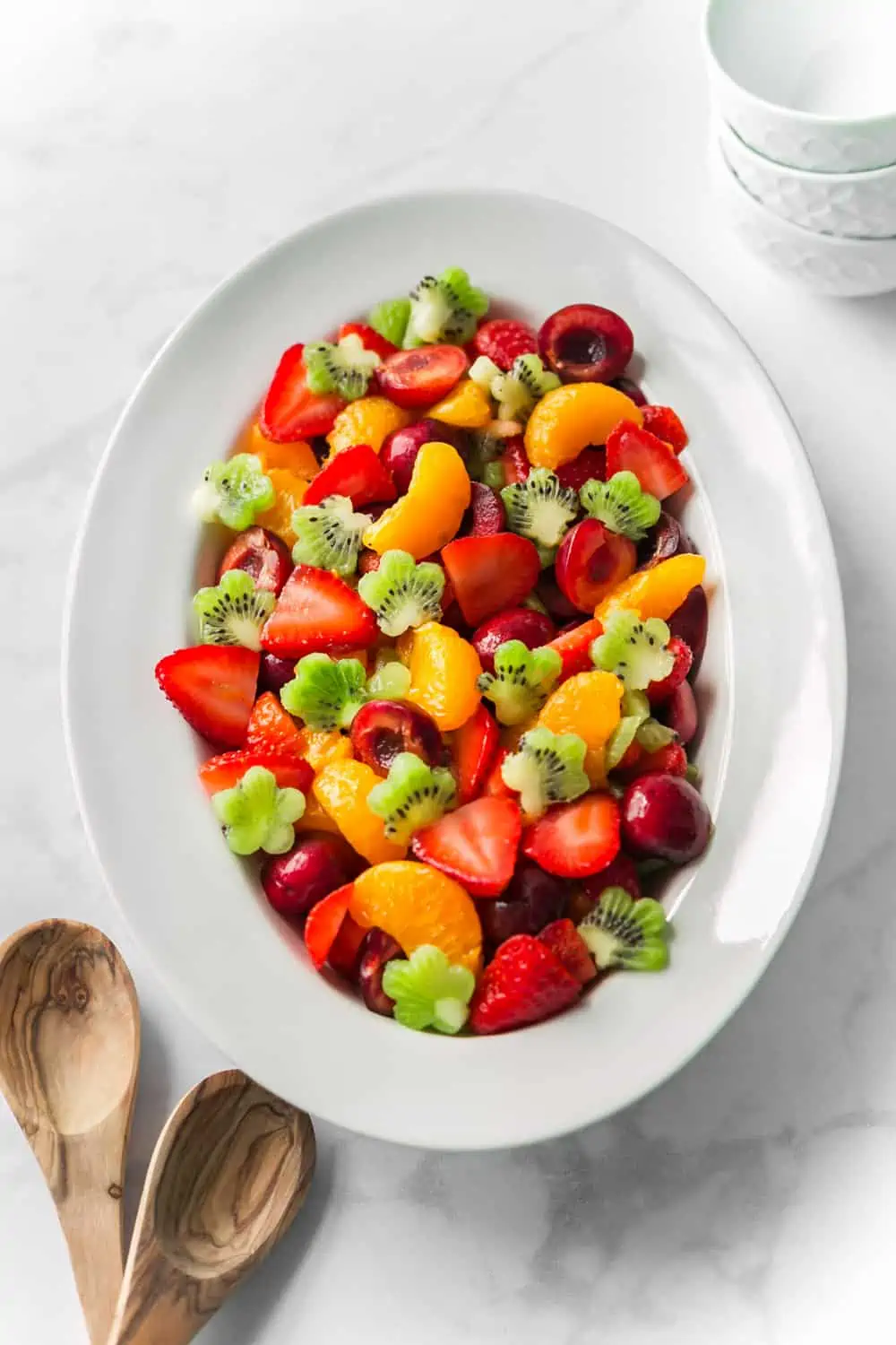 White serving platter with a colorful fruit salad including strawberries, kiwi cut into flower shapes, and mandarin oranges.  