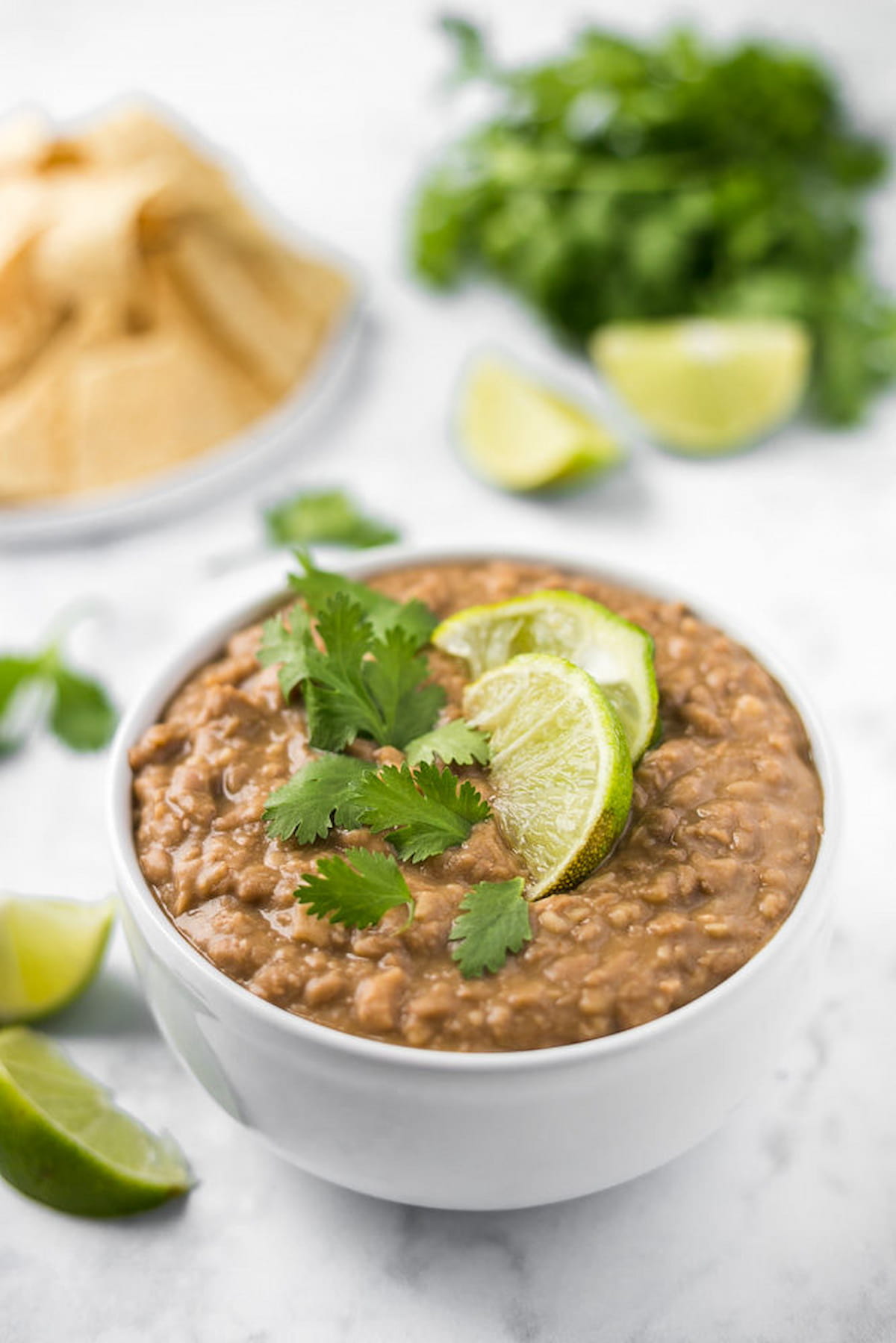 Vegetarian refried beans in a bowl, topped with cilantro le aves and lime wedges.