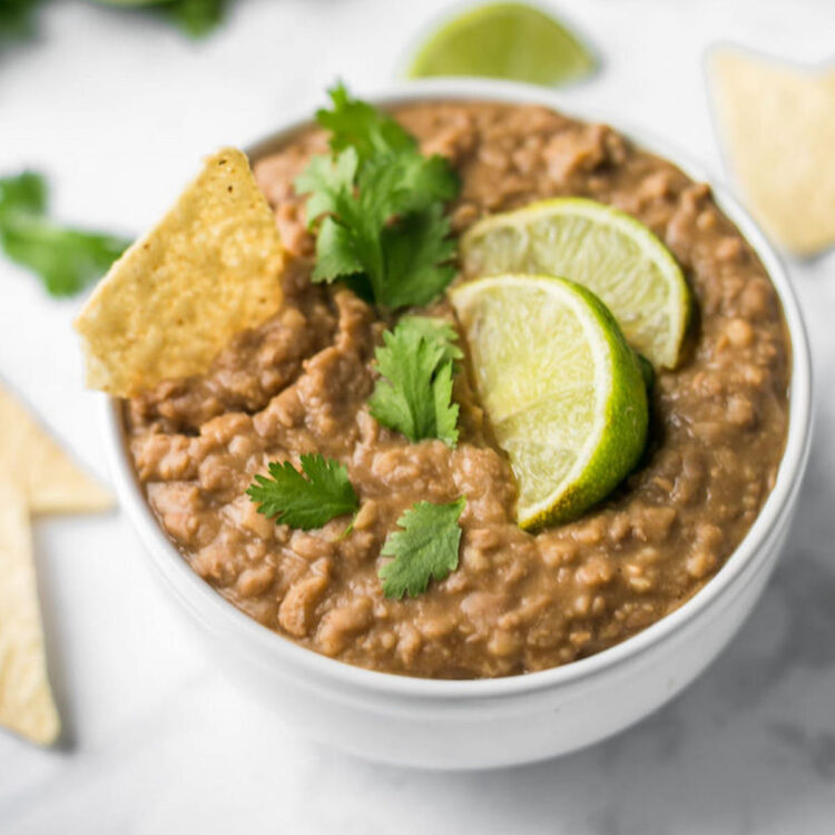 Vegan refried beans in a bowl topped with cilantro leaves and limes wedges.