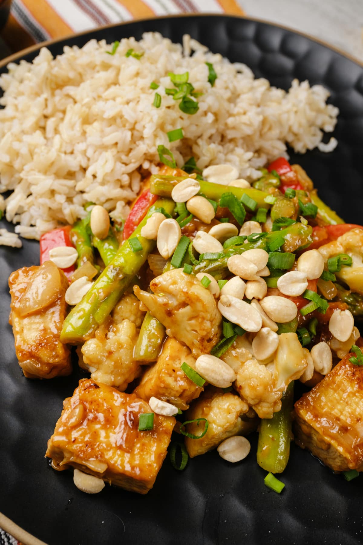 Tofu stir fry with peanut sauce and vegetables served on a plate with a side of rice.