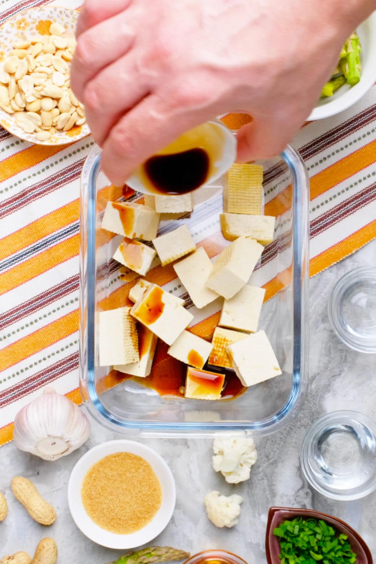 Cubed tofu in a glass container with soy sauce being poured over it.