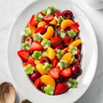 A serving platter of tropical fruit salad with chopped kiwi, mandarin slices, strawberries, and cherries tossed in a sweet and zesty dressing.