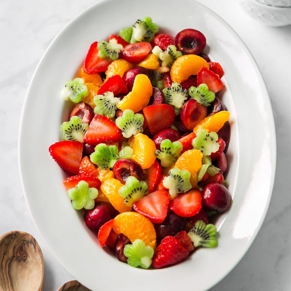 A serving platter of tropical fruit salad with chopped kiwi, mandarin slices, strawberries, and cherries tossed in a sweet and zesty dressing.