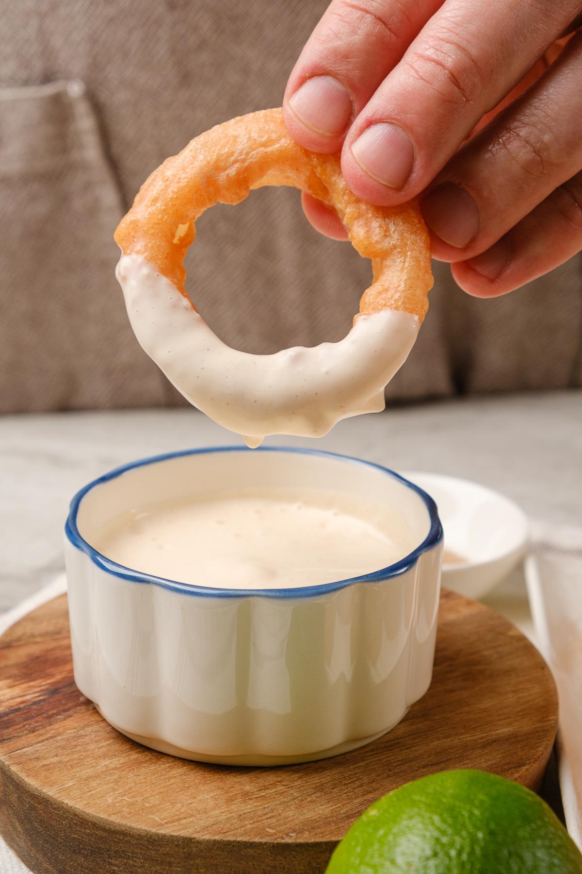 A vegan onion ring being dipped in a homemade vegan mayo sriracha sauce.