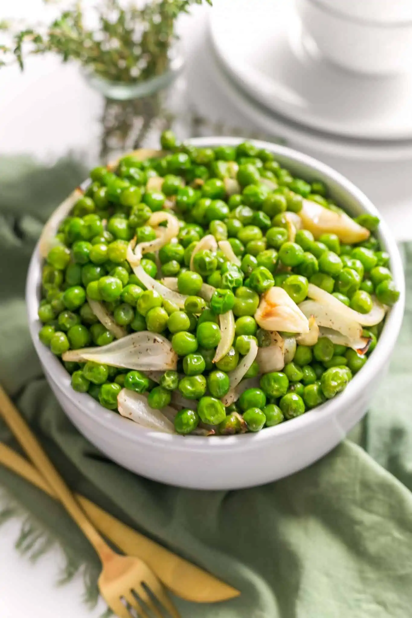 Large white bowl of peas with onions on a green cloth