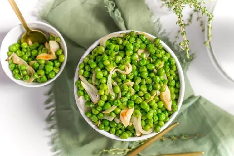 A Large and a medium white bowl of peas with onions on a green cloth
