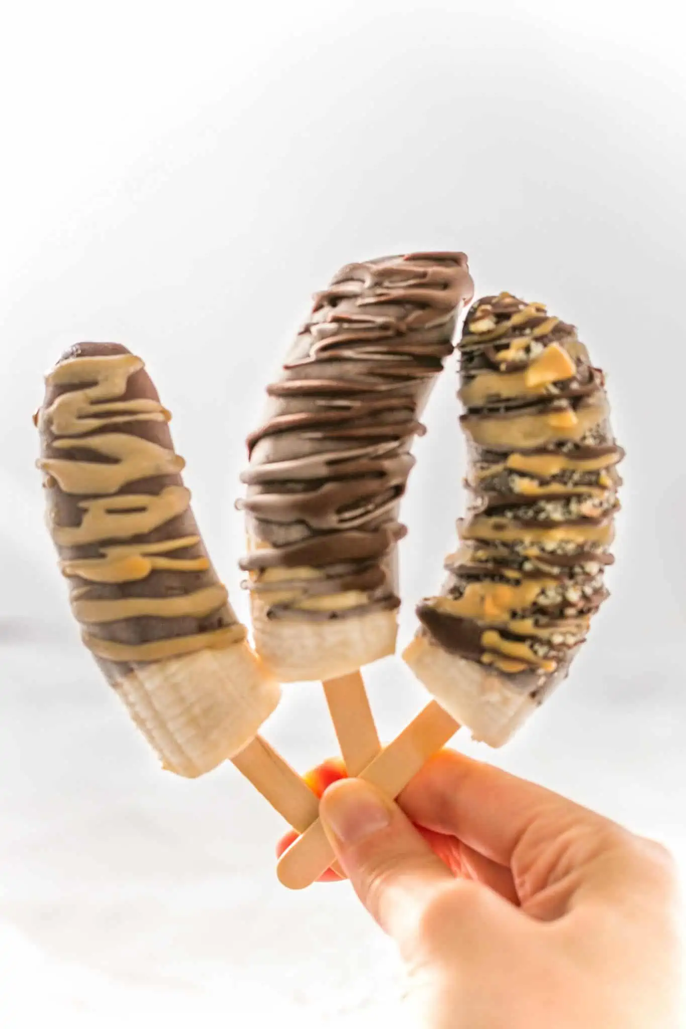 Hand holding three banana popsicles dipped in chocolate.