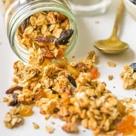 Mason jar filled with homemade granola spilled on white surface.