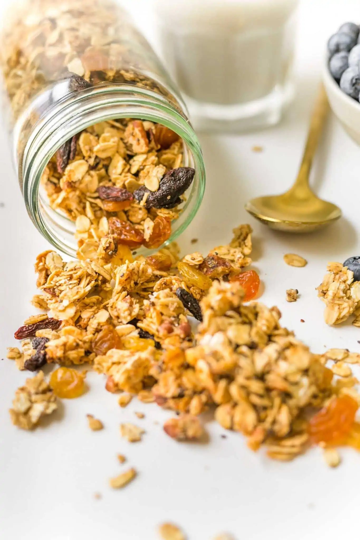 Mason jar filled with homemade granola spilled on white surface