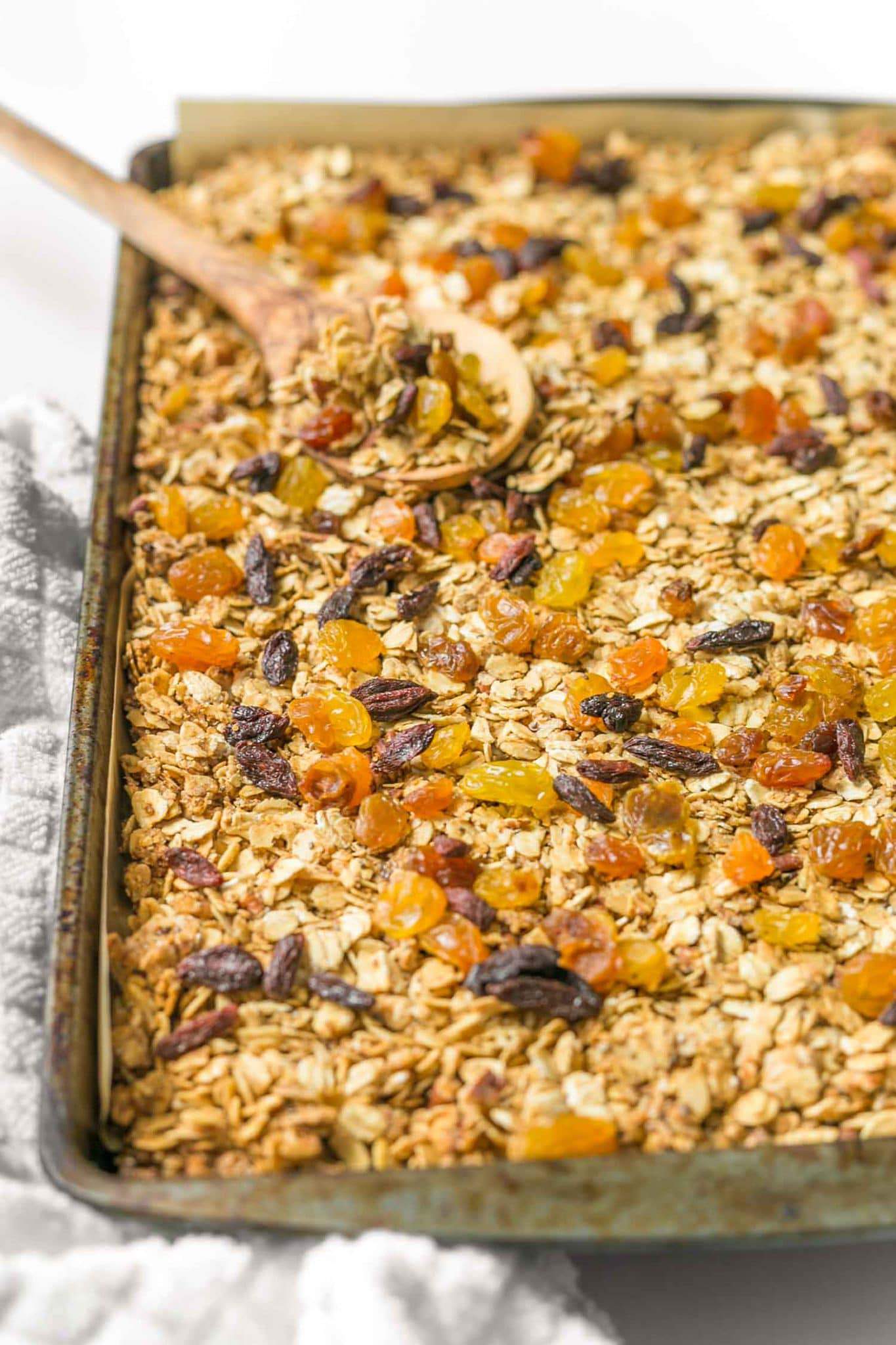 Baking tray with vegan homeamde granola with a large wooden spoon on a white surface 