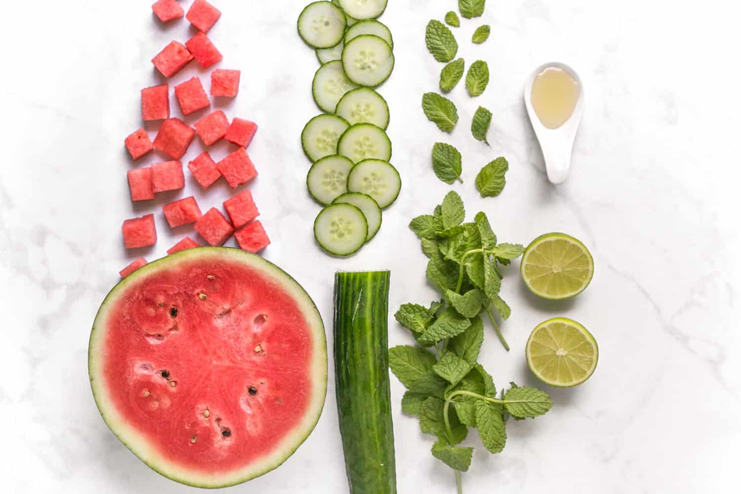 Watermelon cucumber mint lime and agave ingredient flatlay on marble