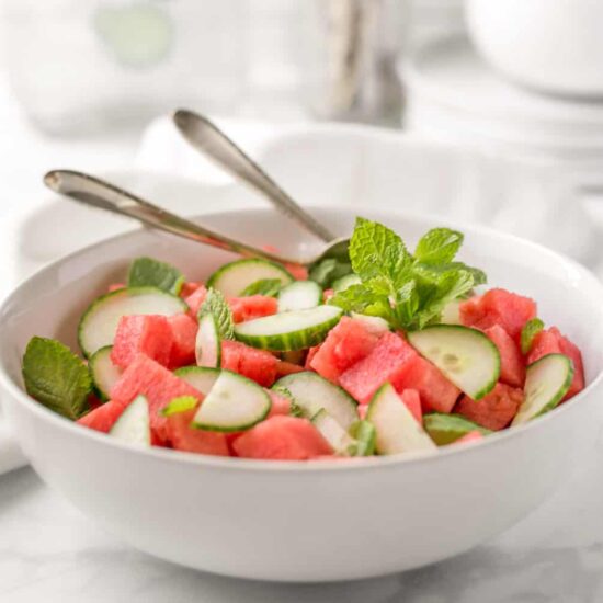 Watermelon cucumber salad in a big serving bowl with serving utensils.