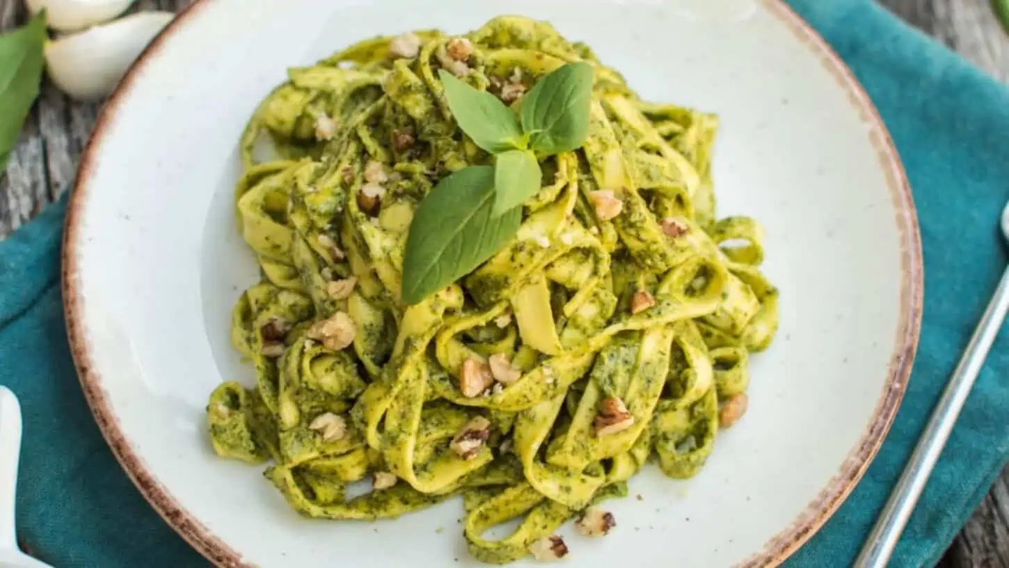 Close up of a neutral dish of vegan walnut pesto pasta with some decorative basil
