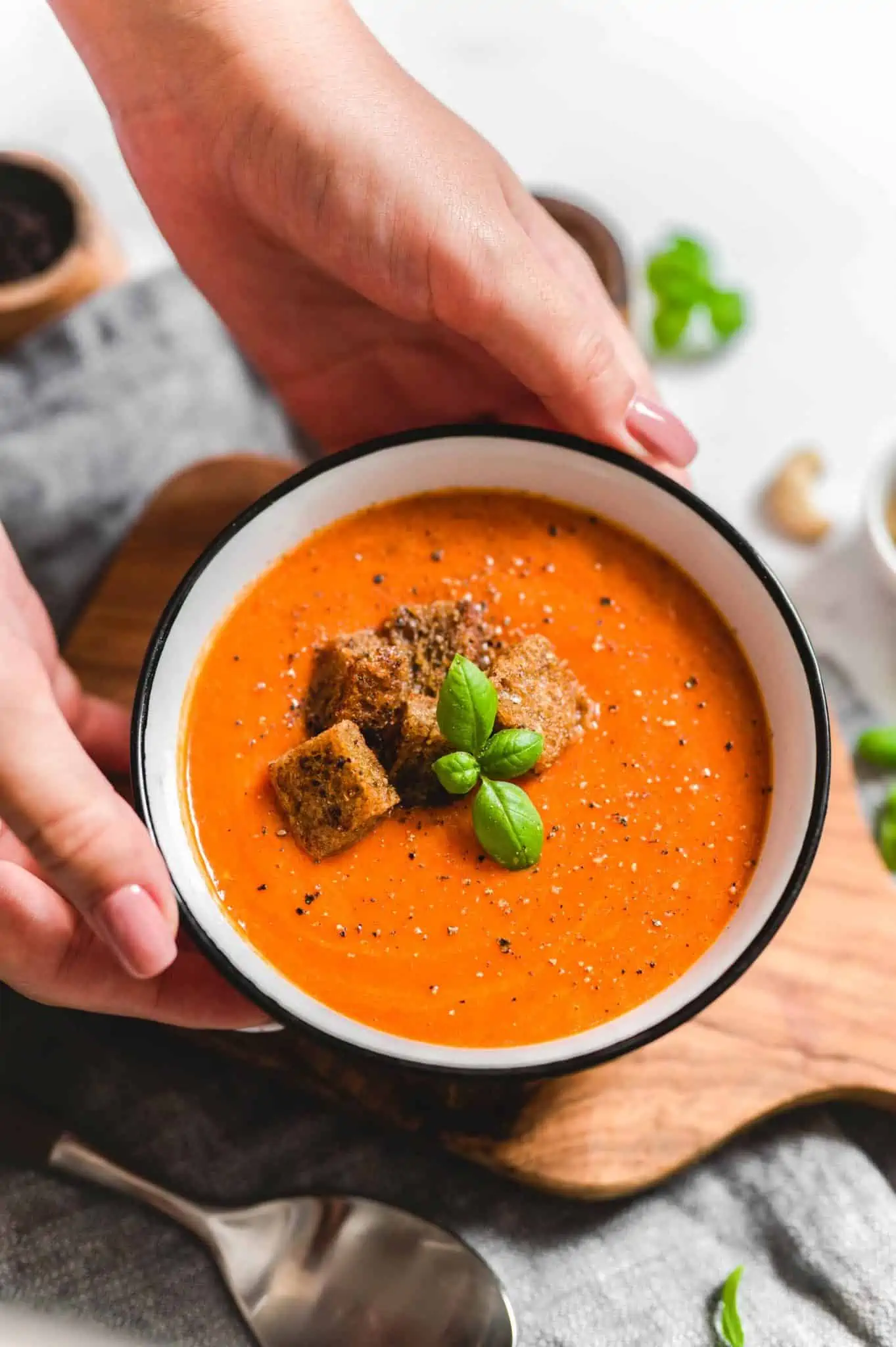 Creamy tomato soup in a bowl topped with croutons, fresh basil leaves, and cracked black pepper.