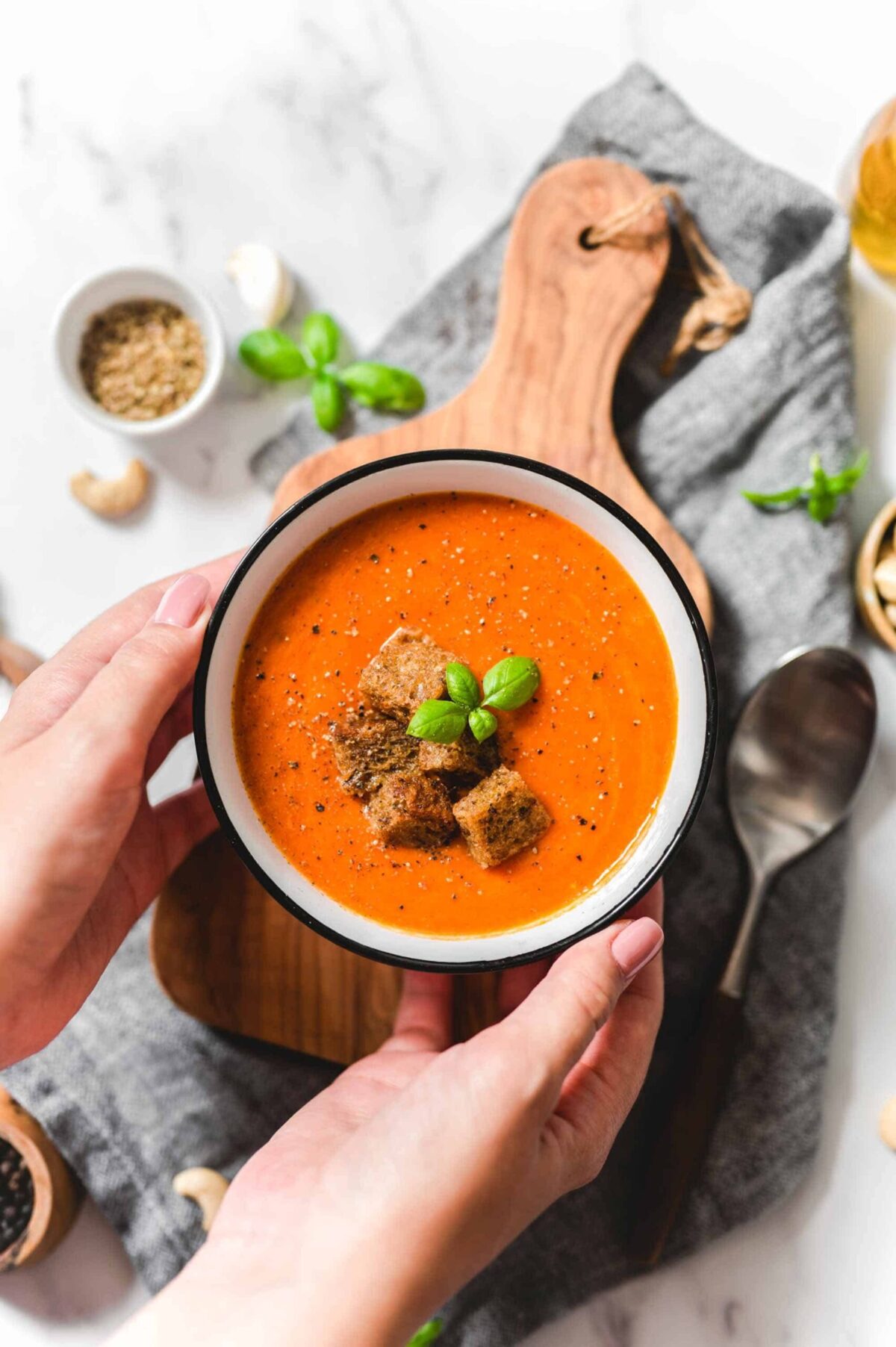 Steaming vegan tomato soup in a bowl with croutons and basil.