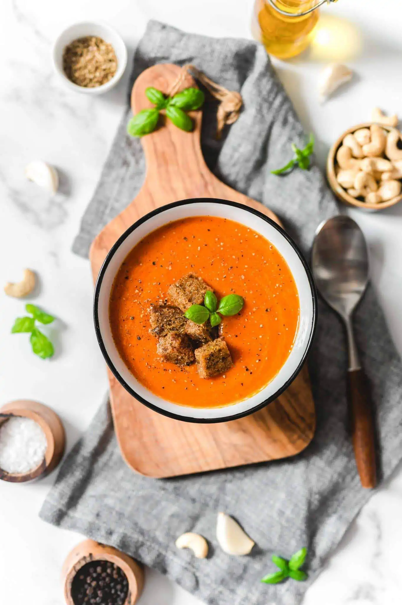 Creamy tomato soup from canned tomatoes in a bowl, topped with croutons and surrounded by ingredients.
