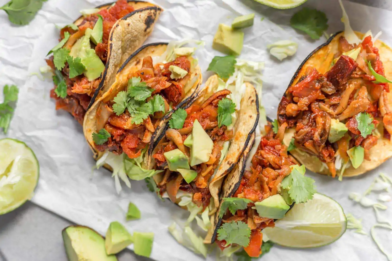 Vegan Shredded Oyster Mushroom Tacos with Chipotle Seasoning with lime slices, avocado, and cilantro.