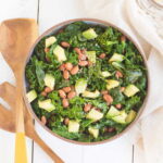 A bowl of cooked kale salad with beans, diced avocado, and sesame seeds.