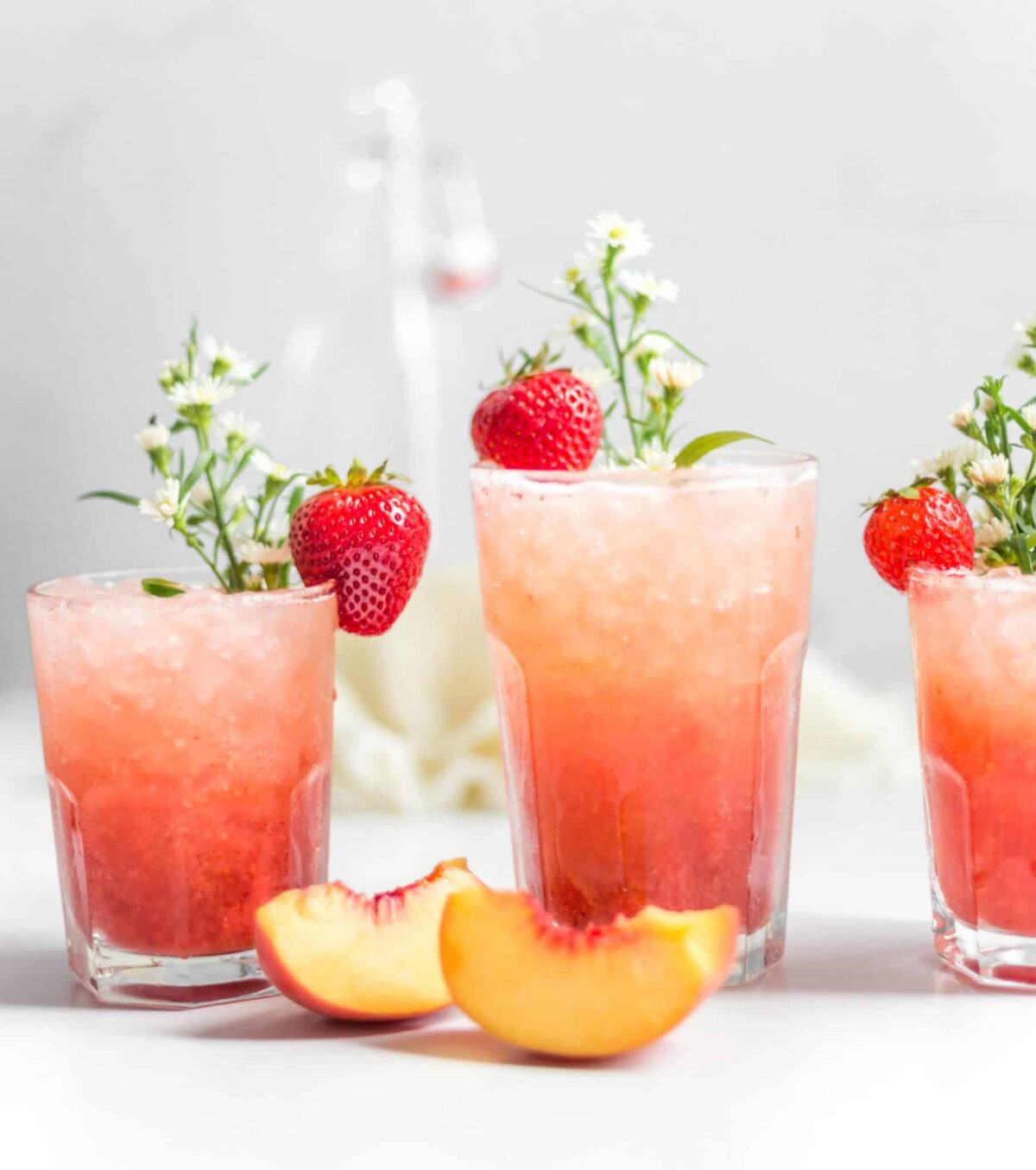 Glasses of fizzy strawberry-peach spritzer garnished with fresh fruit and herbs—refreshing vegan drink.