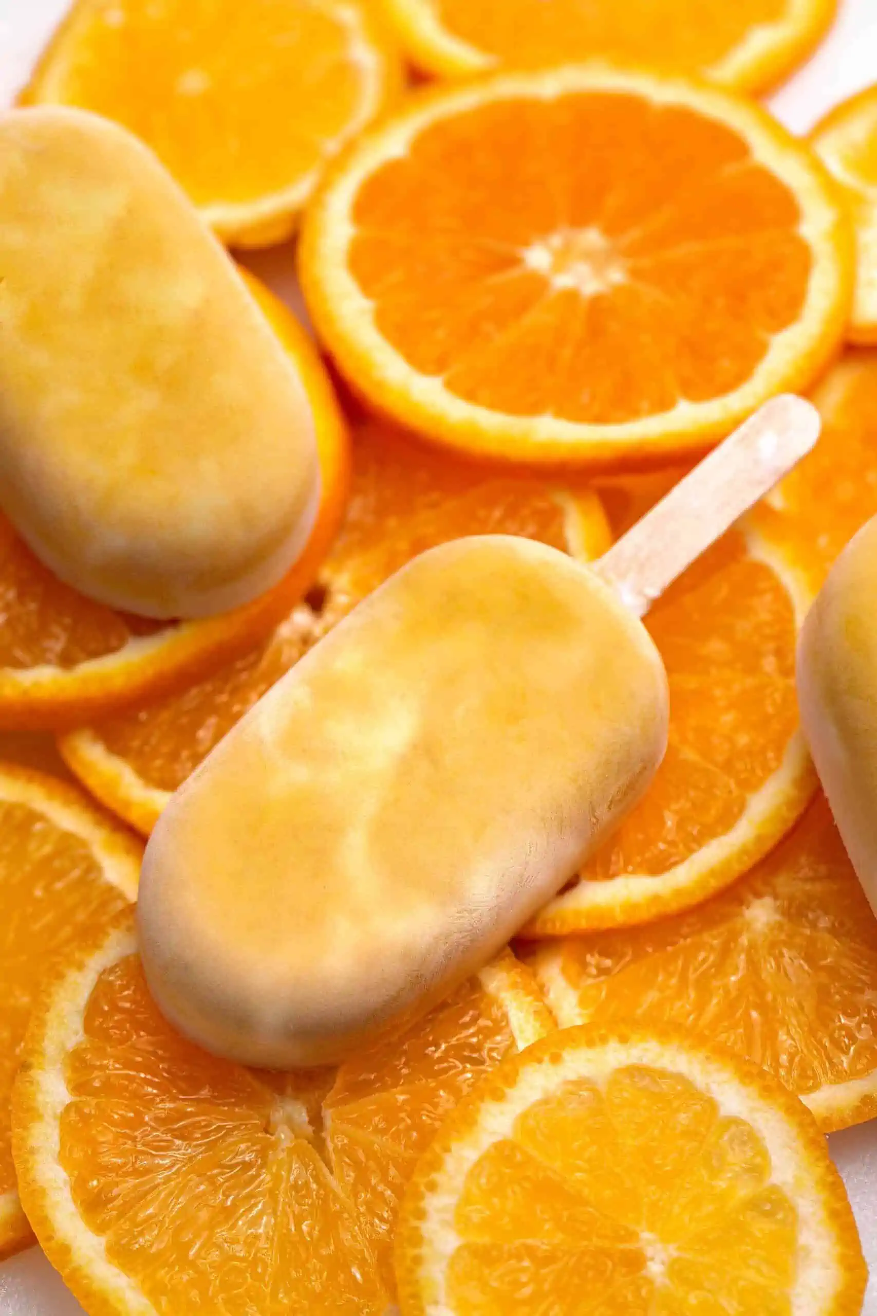 Orange and Cream Vegan Creamsicle Ice Cream Bars On Top of a Pile of Sliced Oranges