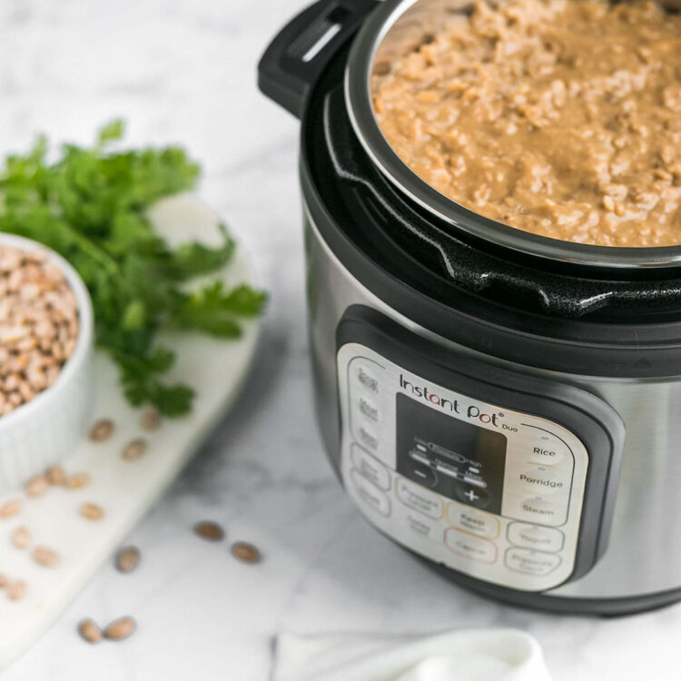 An Instant Pot filled with refried beans, next to a bowl of dried pinto beans.
