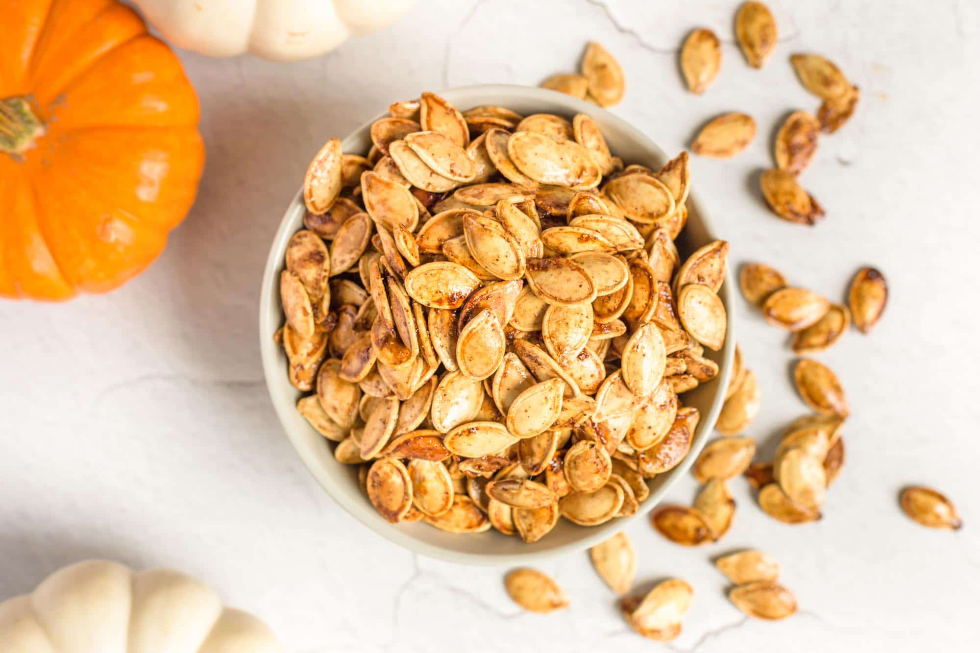 Sweet Roasted Pumpkin Seeds With Pumpkin Spice in an over filled bowl with pumpkin decor beside.
