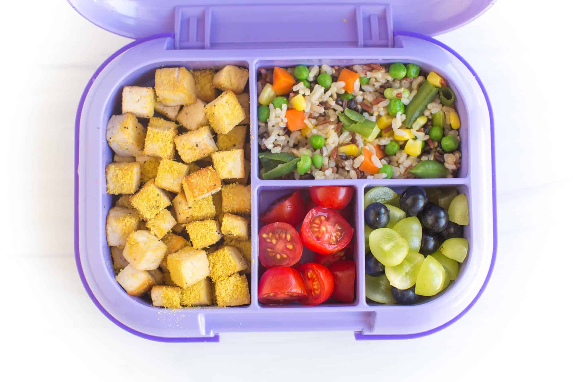 Vegan school lunch with seasoned tofu, whole grain rice, and colorful vegetables.