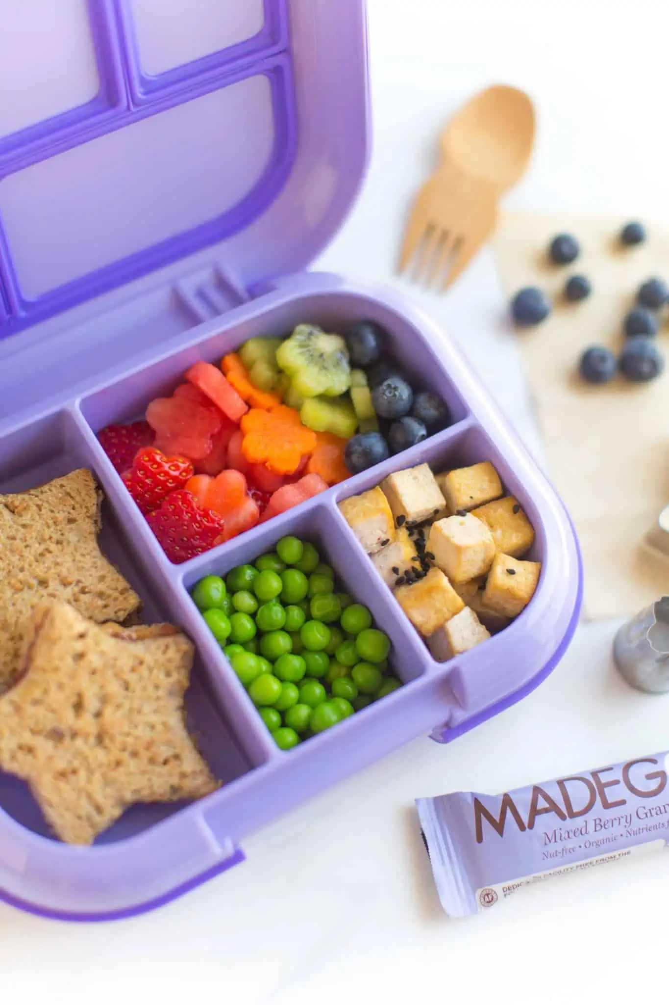 Purple kids lunchbox with vegan food including tofu, peas, veggies, peanut butter and jelly sandwich. 