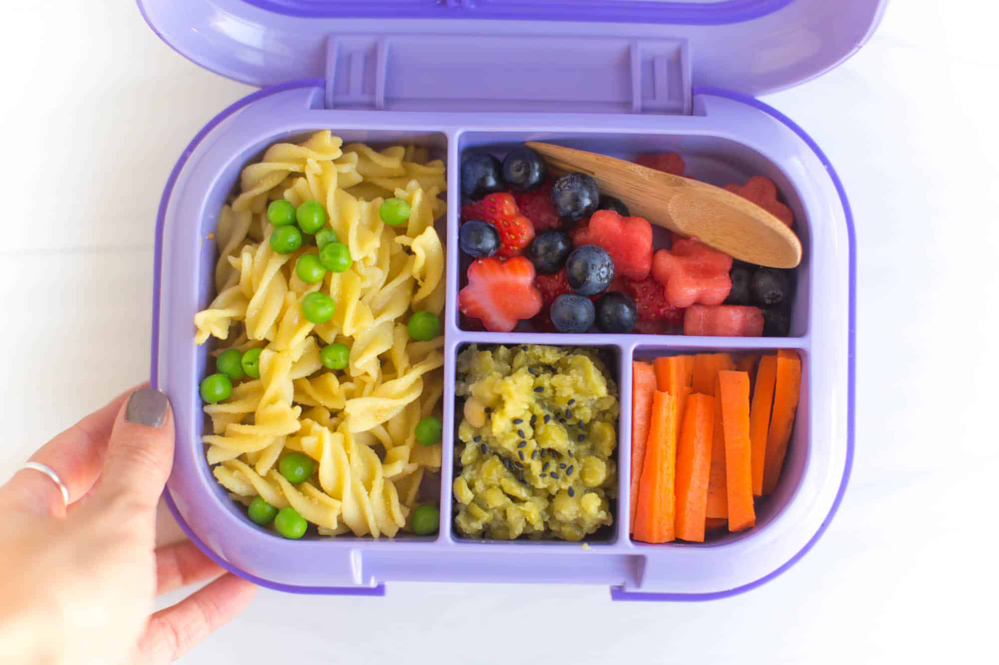 Vegan pasta lunch with peas and flower-shaped fruit salad in a school lunchbox.