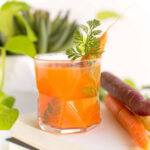 Carrot juice cocktail in a glass, garnished with fresh herbs and sitting beside a few raw carrots.
