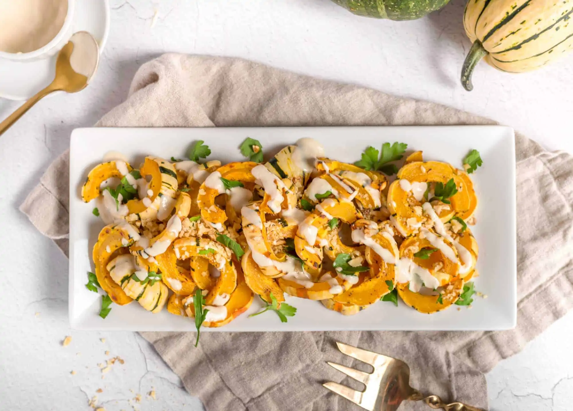 A plate of roasted delicata squash drizzled with dressing and garnished with parsley.