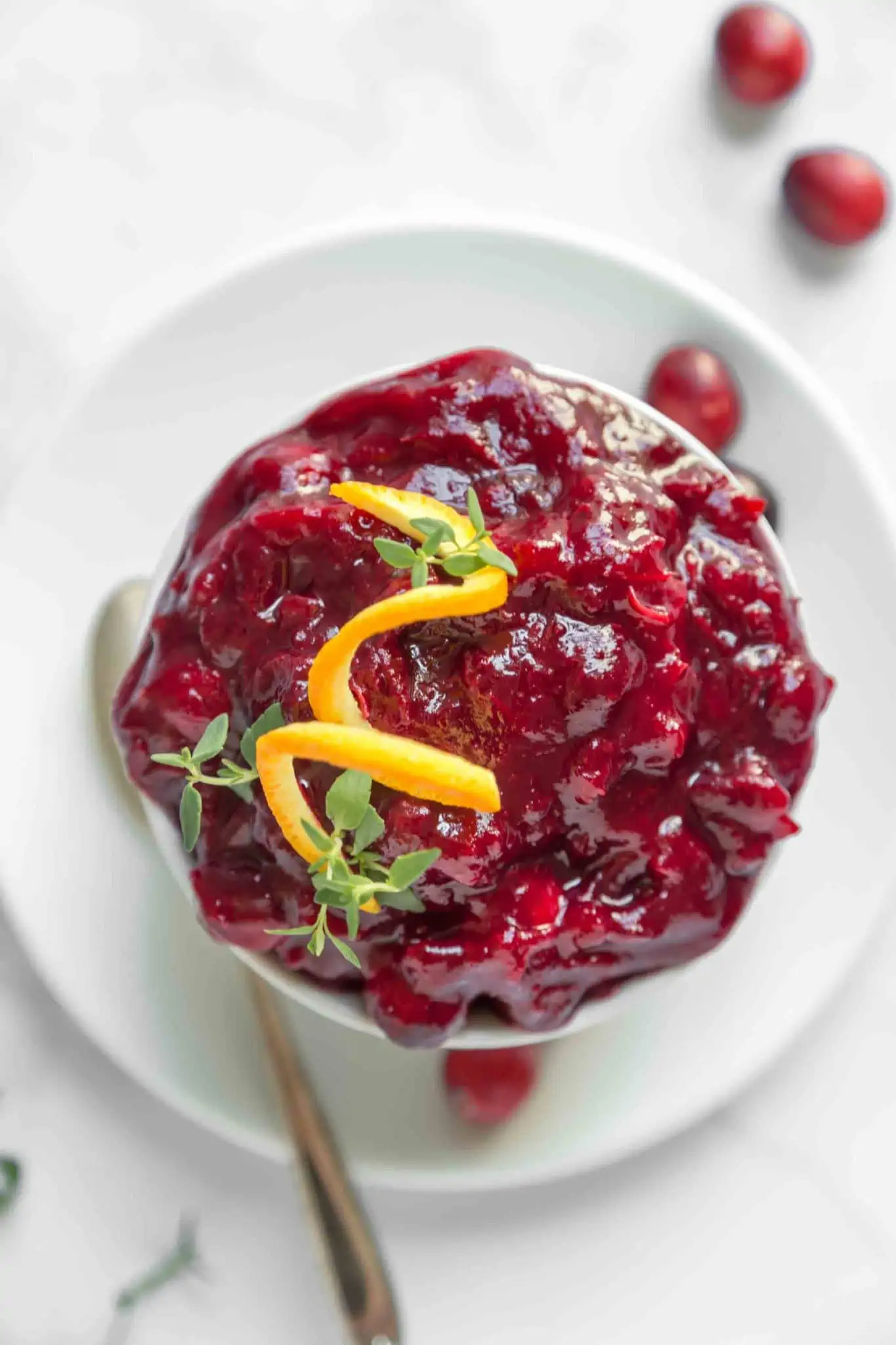 A close-up of a bowl of homemade orange cranberry sauce recipe from World of Vegan with garnish of orange peel. 