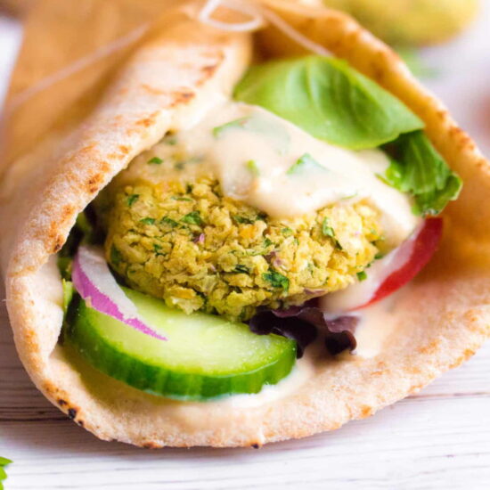 Falafel pita sandwich filled with golden falafels, sliced cucumber and red onion, and a tahini dressing.