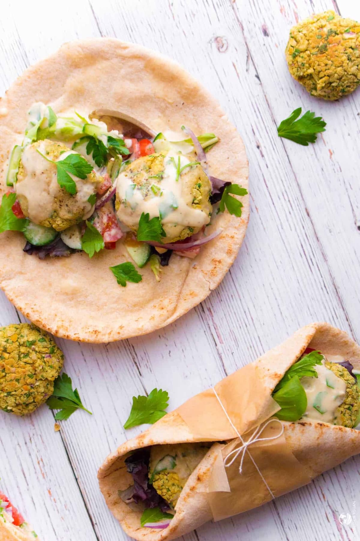 Two falafel pita sandwiches on a wooden table top.