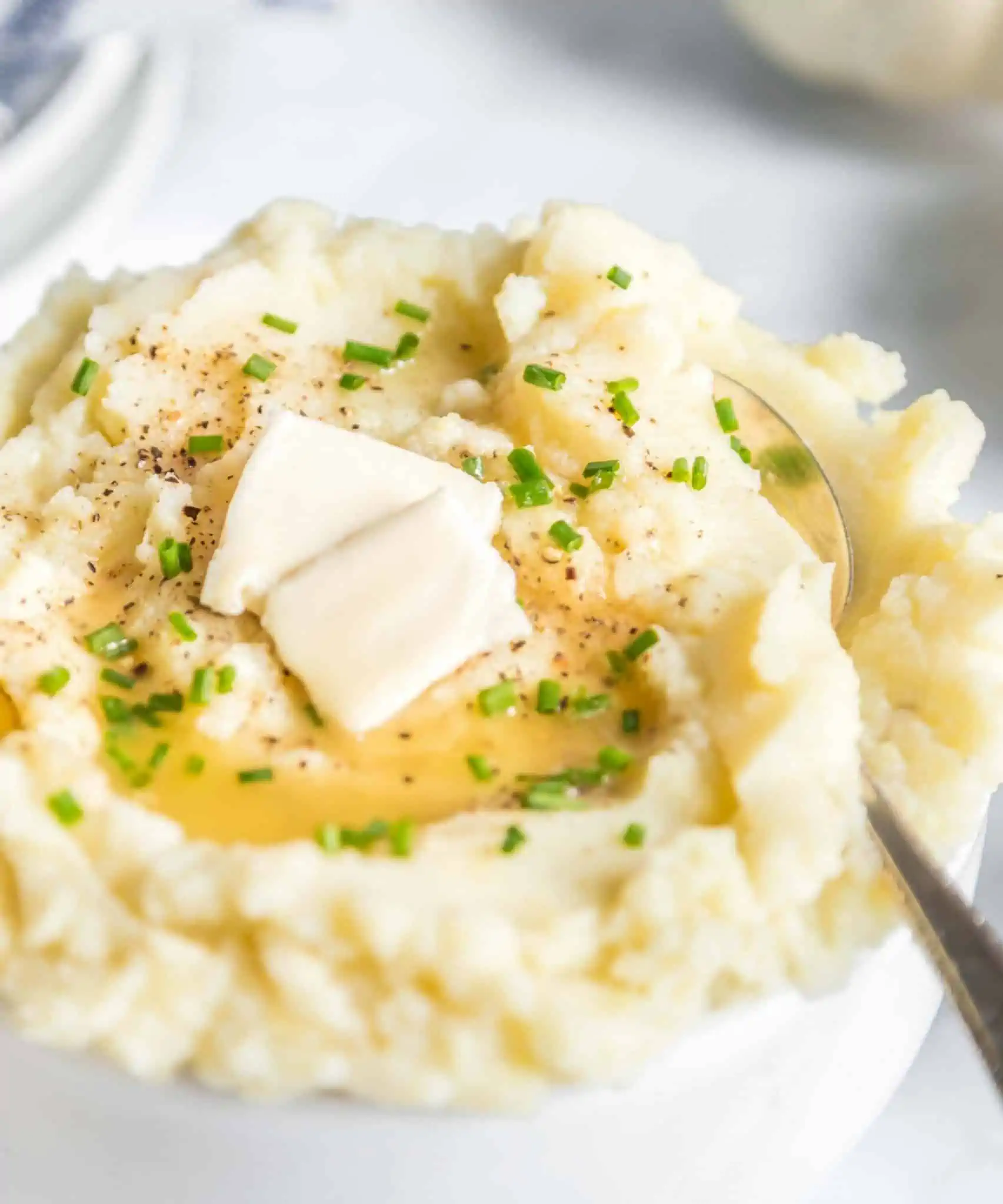 Dairy-free mashed potatoes in a bowl with serving spoon and topped with vegan butter.