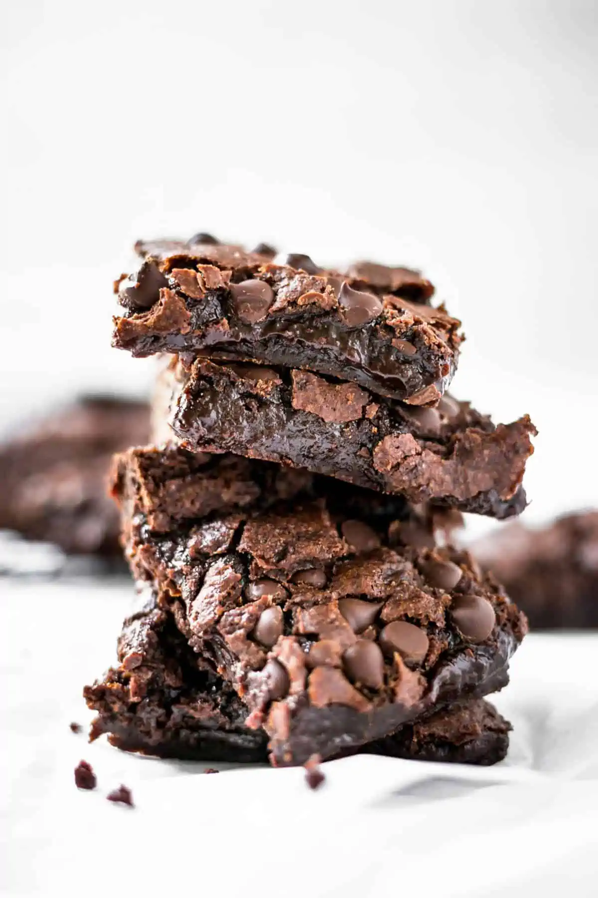 Four squares of vegan brownies stacked with chocolate chips sprinkled around.