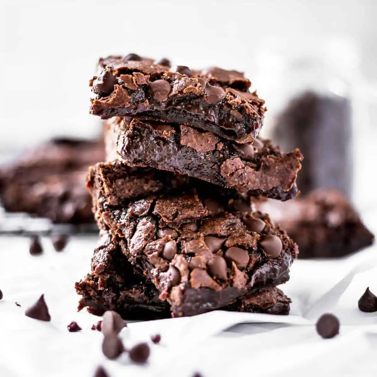 Four squares of vegan brownies stacked with chocolate chips sprinkled around.