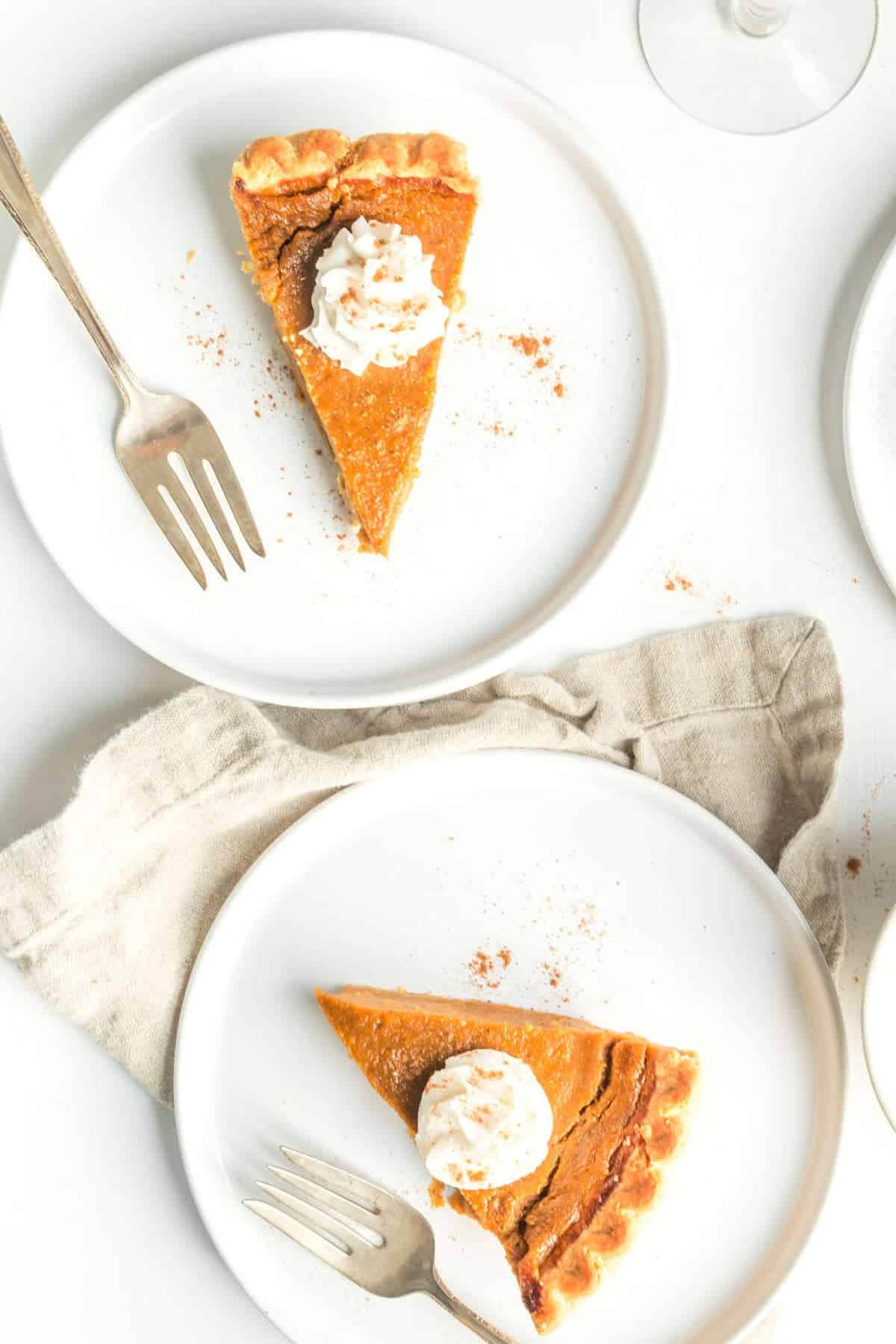 Two slices of vegan pumpkin pie on plates and served with vegan whipped cream.