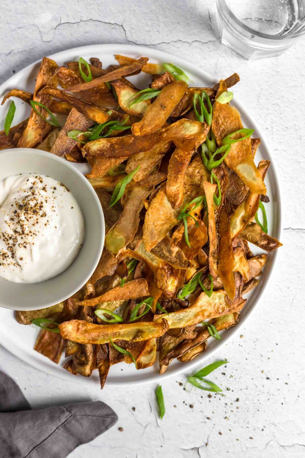 A platter of potato skins chips served with a creamy dip and topped with sliced green onions.