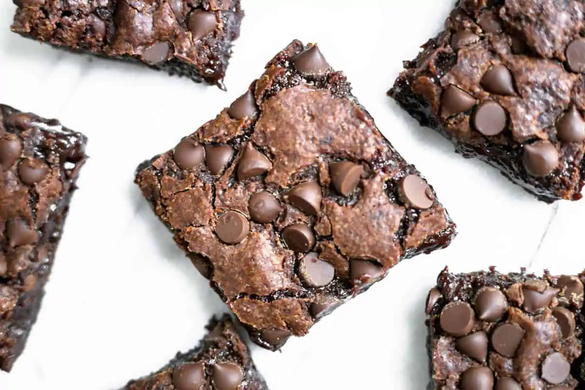 Vegan brownie squares on a light background, topped with chocolate chips.