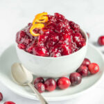 A bowl of vegan cranberry sauce topped with a spiraled orange peel.