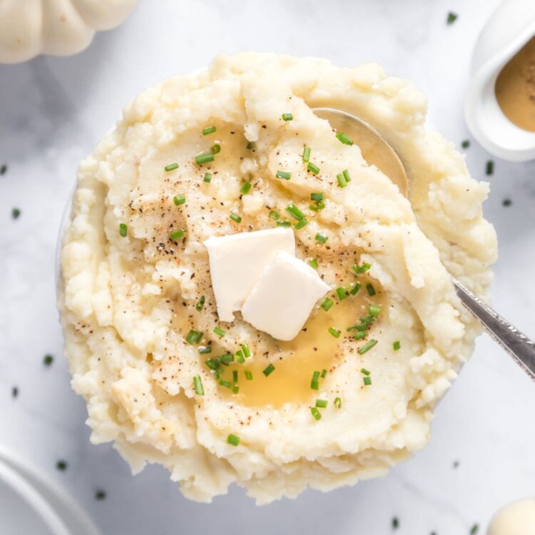 A big bowl of creamy vegan mashed potatoes with garlic, a sprinkle of chives, and gravy on the side.