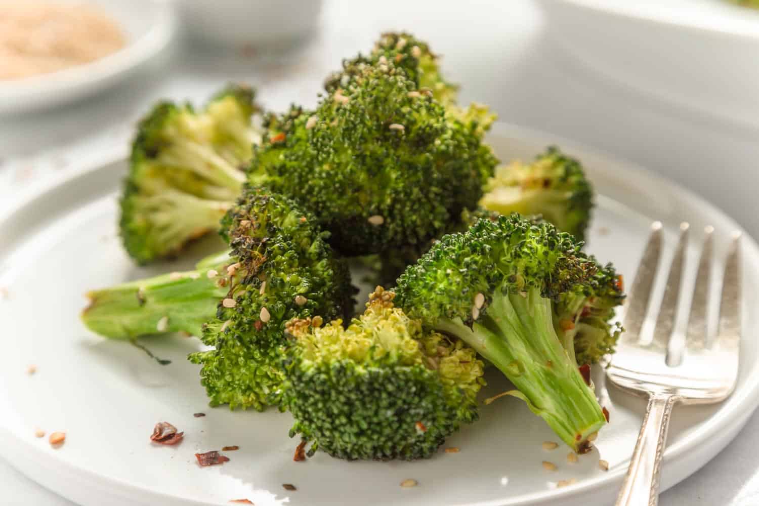 Air fried broccoli sprinkled with sesame seeds served on a white plate with a rustic fork