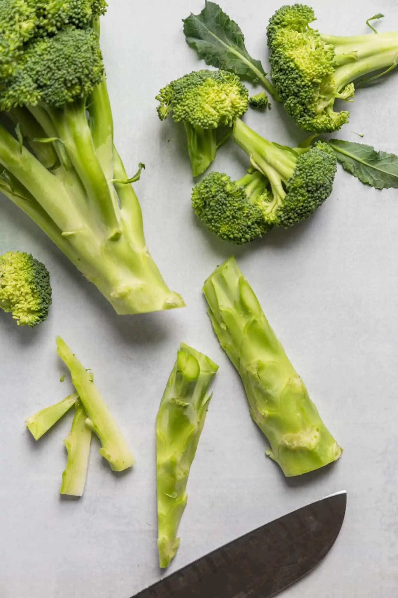 Broccoli stalks chopped on a cutting board with a chefs knife