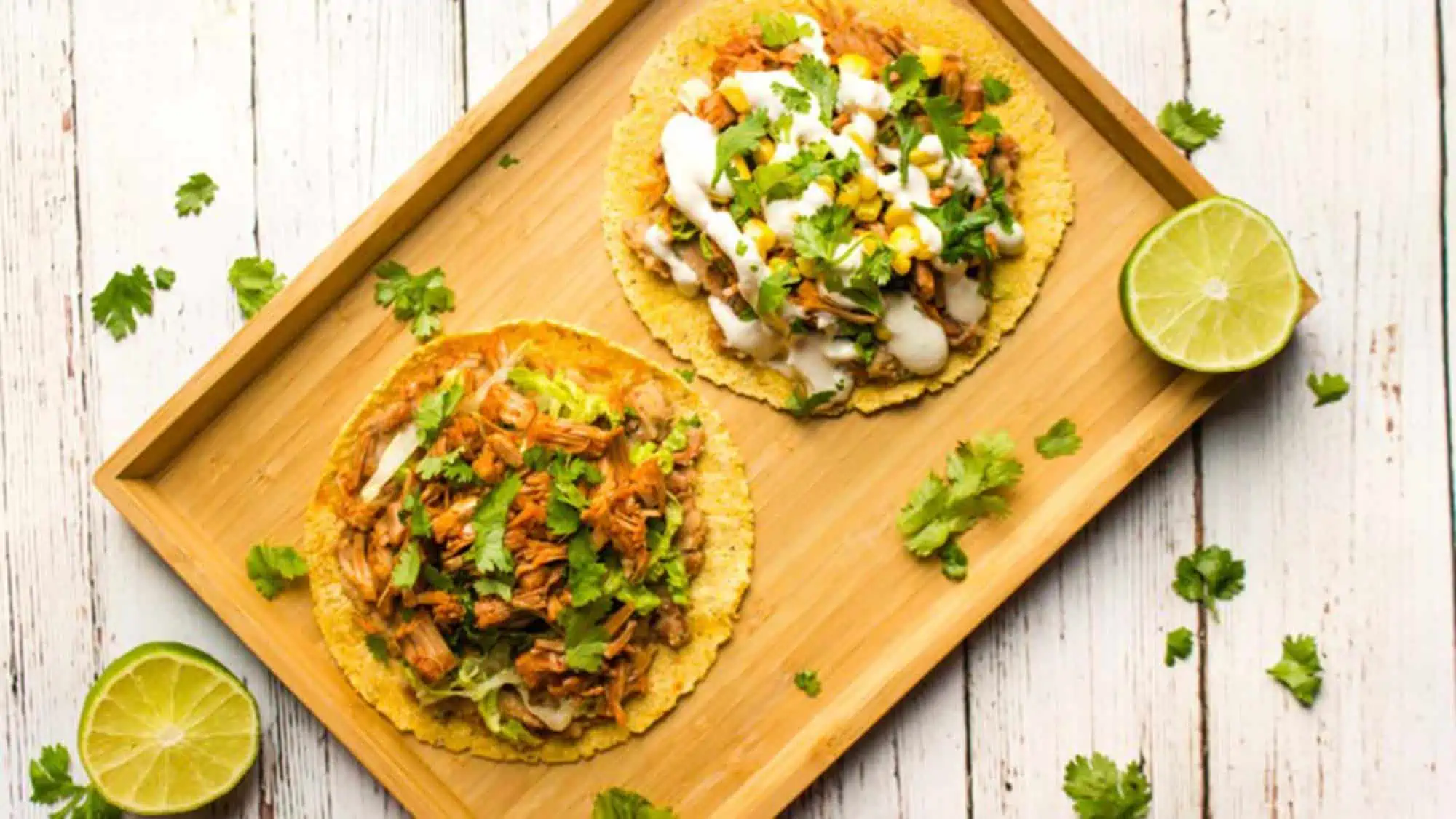 Jackfruit tostadas on a wood serving board topped with cilantro and vegan crema and corn on corn tortillas.