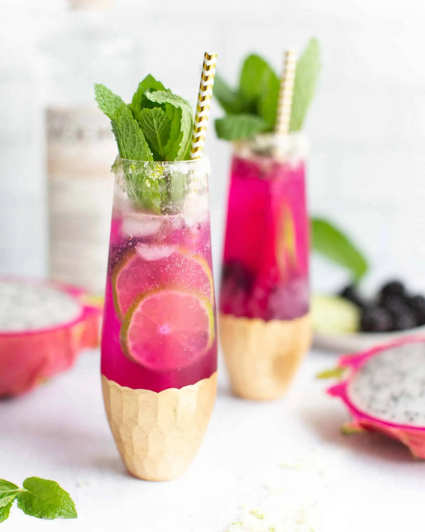 Pink cocktail in an elegant glass with mint garnish and a gold striped paper straw.