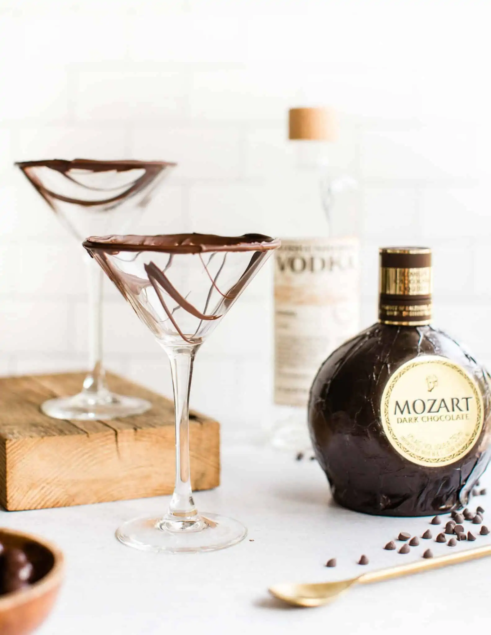 Martini glasses drizzled with vegan chocolate next to Mozart Dark Chocolate Liqueur and Koskenkorva Vodka and a gold spoon.