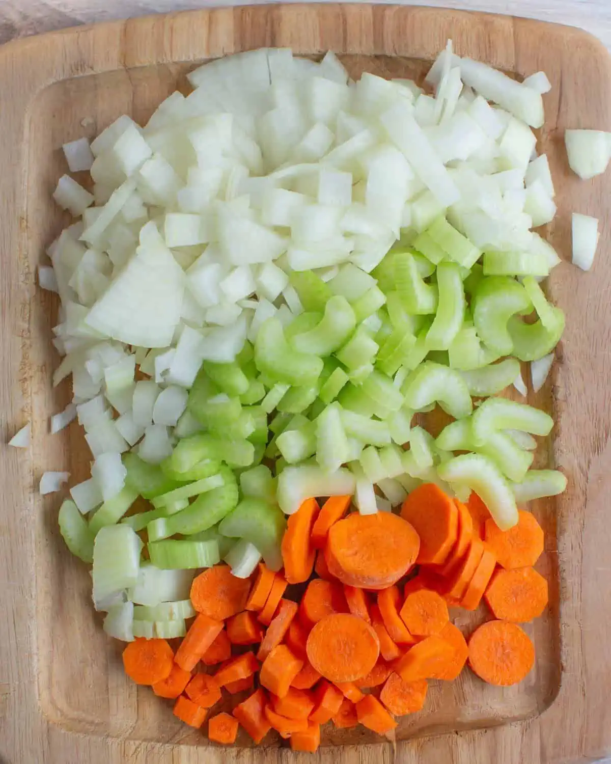 Wooden cutting board with diced onion, celery, and carrots. 